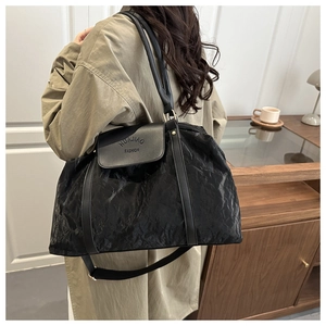 Detail of black tote bag with wrinkled texture, leather flap, and long shoulder strap