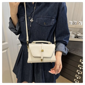 Detail of minimalist beige leather crossbody bag with cylindrical gold clasp on model