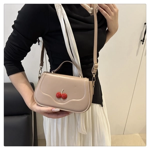 Detail of light beige crossbody bag featuring cherry metal clasp and rounded top handle