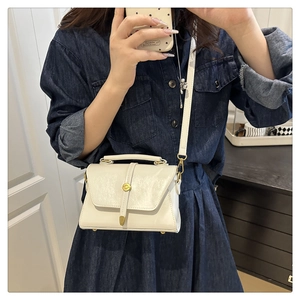 Close-up of a cream crossbody bag with a gold buckle and adjustable strap on a model