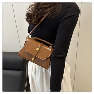 Detail of glossy brown leather crossbody bag with gold metallic shield buckle decoration