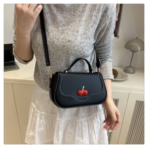 Detail of black PU leather shoulder bag featuring decorative red cherry and gold hardware