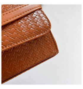 Gros plan détaillé sur la texture du cuir tressé marron et les coutures du sac à bandoulière