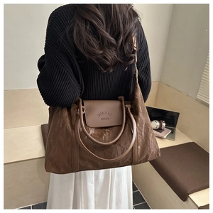 Detail of dark brown wrinkled texture tote bag with embossed brand logo on the magnetic flap