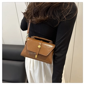Close-up of brown polished crossbody bag with gold round buckle shown on a model