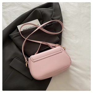 Detail of light pink leather crossbody bag with gold hardware on a grey blazer fabric