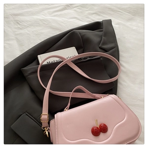 Detailed view of pink leather crossbody bag featuring a cherry metallic clasp on white fabric