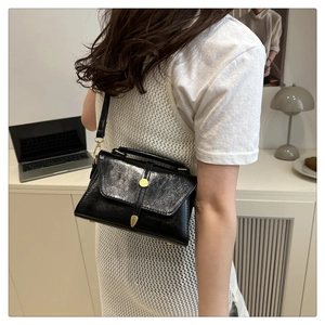 Detail of black wrinkled texture crossbody bag with gold round clasp and slim shoulder strap
