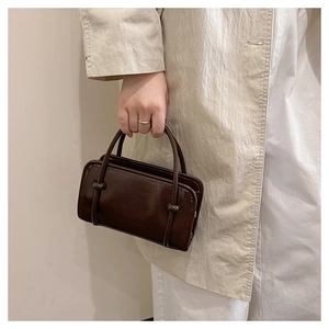 Detail of dark brown mini Boston bag with decorative knot and polished leather texture