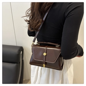 Detail of dark brown glossy crossbody bag with golden round turn-lock buckle and handle