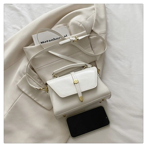 Detail of ivory faux leather handbag with gold round buckle and adjustable shoulder strap