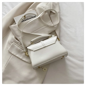 Detailed view of white leather crossbody bag with gold hardware on white textured bedding