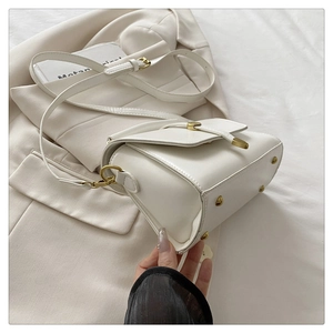 Detail of white vintage crossbody bag with gold buckle and adjustable strap on a blazer