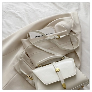 Close-up of cream leather handbag with gold hardware on a stylish beige blazer