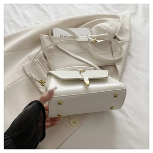 Detailed view of the white leather handbag featuring gold bottom studs and premium hardware