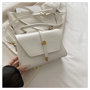 Detailed view of cream white crossbody bag with gold round lock on white blazer