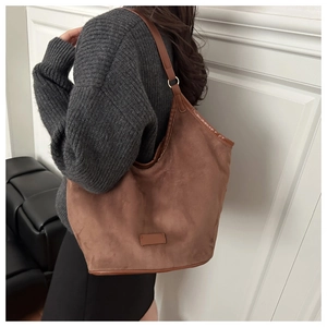 Model wearing a large brown suede tote bag with slim shoulder straps and square detail