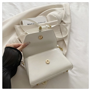 Detail view of cream white flap bag with golden magnetic clasp and bottom studs