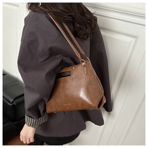 Detail view of brown PU leather shoulder bag with oval handle and gold rivets worn by a model