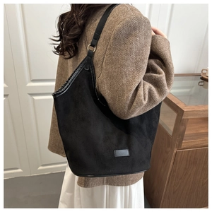 Minimalist black matte suede bucket bag shown on shoulder over a brown blazer