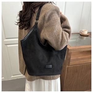 Close-up of black suede tote bag with metal rings on a model in a brown blazer