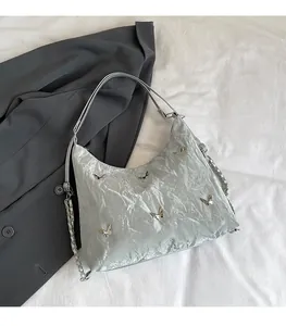 Detail of silver pleated shoulder bag featuring metallic butterfly charms and chain strap