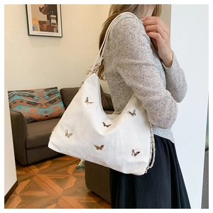 Detail of white moon-shaped shoulder bag with metallic butterfly accents on model