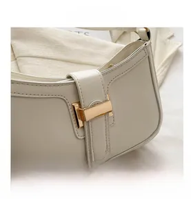 Close-up of golden rectangular metal buckle and neat stitching on white leather bag