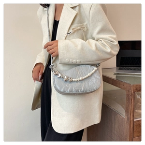 Detail of silver pleated crescent bag with decorative pearl and heart chain strap