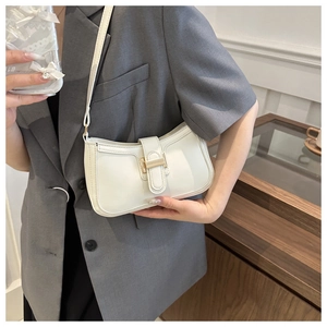 Detail of a beige crescent bag with a gold T-shaped clasp on a woman's shoulder