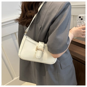 White faux leather crescent bag worn as a shoulder bag on model with gold metal buckle detail