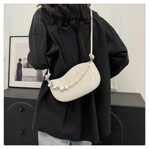 Detail of cream white underarm bag with pearl and silver heart chain on black shirt