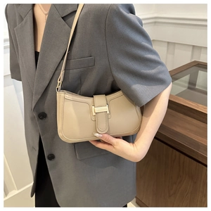Detail of apricot crescent bag with gold buckle worn with a gray blazer in minimalist setting