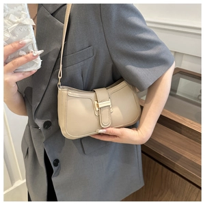 Detailed shot of beige crescent bag with gold buckle and fine stitching on a grey blazer