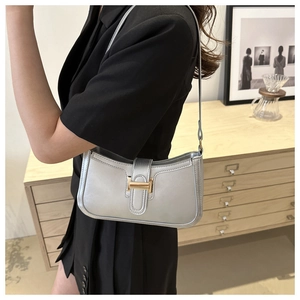 Close-up of a silver crescent shoulder bag with a gold H-shaped hardware buckle