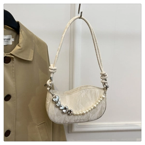 Detail of ivory crescent bag featuring heart pendant, pearls, and braided strap