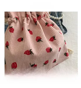 Detail of pink corduroy drawstring bag featuring cute strawberry pattern and pearl strap