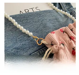 Detail of pink strawberry corduroy bucket bag featuring pearl strap and gold hardware