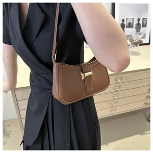 Caramel leather crescent bag with golden buckle shown on shoulder in cozy interior