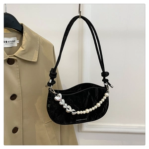 Detail of black glossy crescent bag featuring pearl and silver heart chain on trench coat