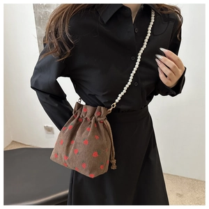 Detail of brown corduroy bucket bag featuring red strawberry embroidery and pearl strap
