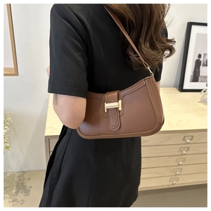 Brown faux leather shoulder bag with gold buckle worn on the shoulder with a black dress
