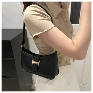 Detail of vintage black crescent bag featuring gold H-shaped buckle on a model shoulder