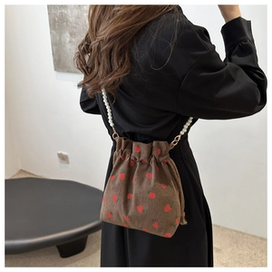 Detail of strawberry corduroy bucket bag with elegant white pearl beaded strap