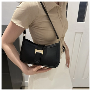 Detail view of a black crescent underarm bag with gold H-buckle worn by a model