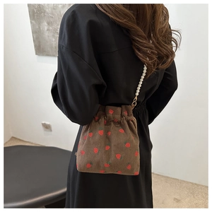 Detail of a brown corduroy strawberry bucket bag with white pearl beaded shoulder strap