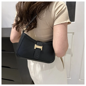 Detail of black crescent shoulder bag with golden H-buckle on a female model