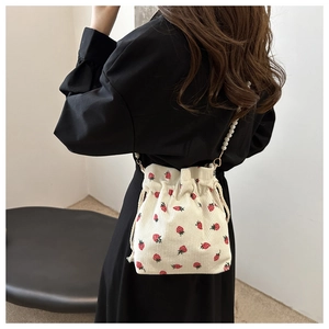 Detail of off-white corduroy bucket bag with strawberry print and pearl chain strap