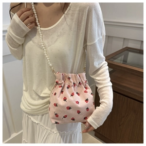 Detail of pink corduroy bucket bag featuring strawberry prints and a pearl strap