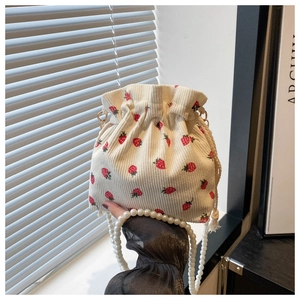 Detail of strawberry print corduroy bucket bag with pearl handle and woven drawstring